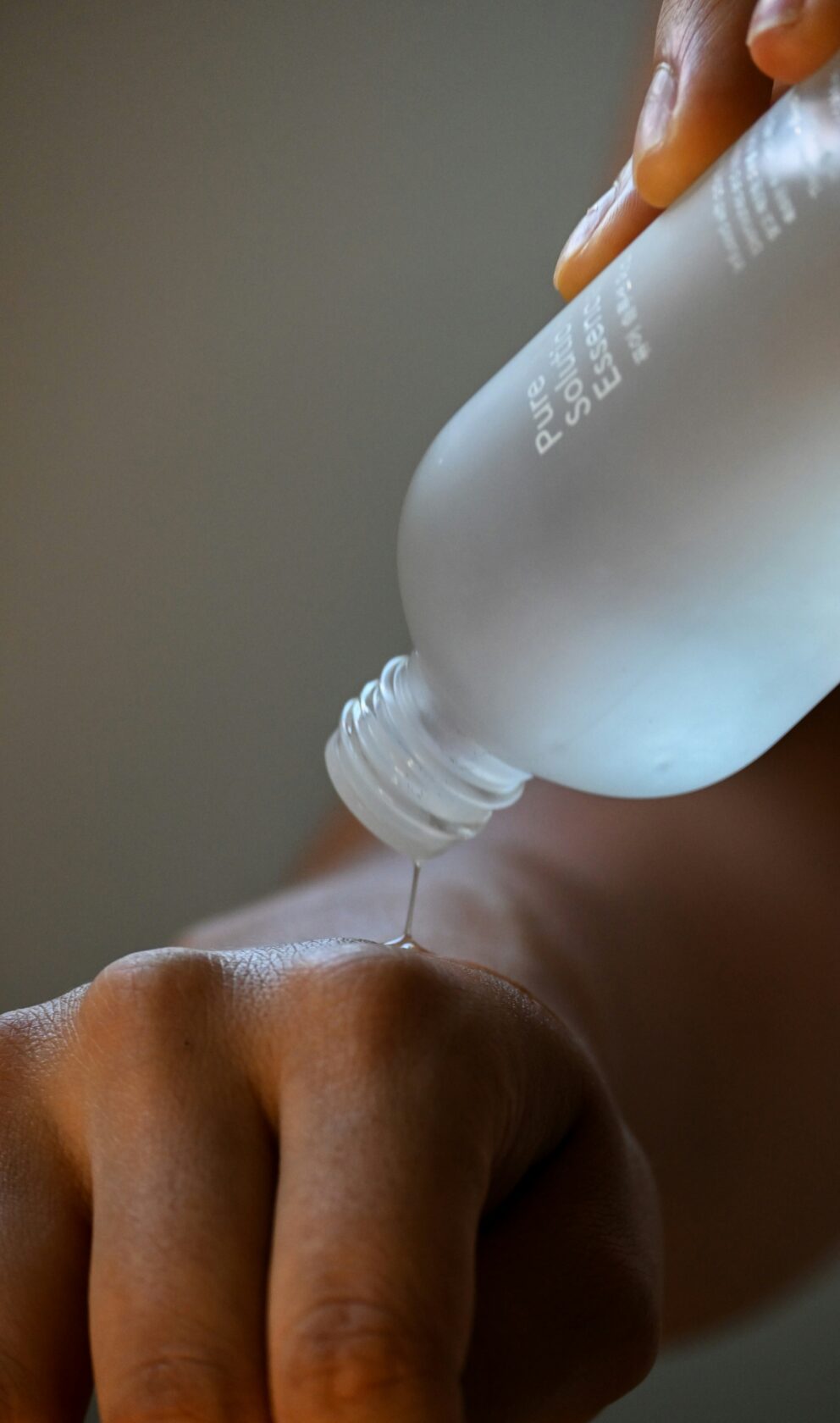 Applying Skincare Essence A hand pouring a clear essence from a glass bottle onto the skin of another hand.