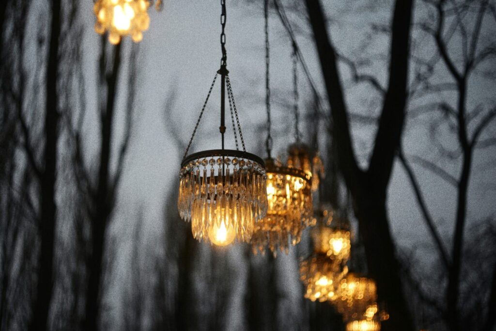 Several ornate chandeliers hanging from tree branches, illuminated against a dusky sky.