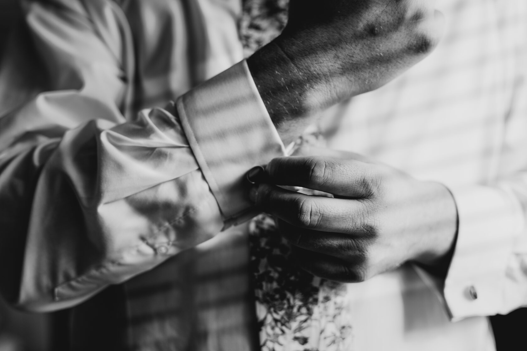 Groom Preparing for Wedding in Black and White A close-up of a man's hands buttoning his shirt cuff while preparing for a special occasion, featuring a patterned tie. Shot for Lydia Turner.