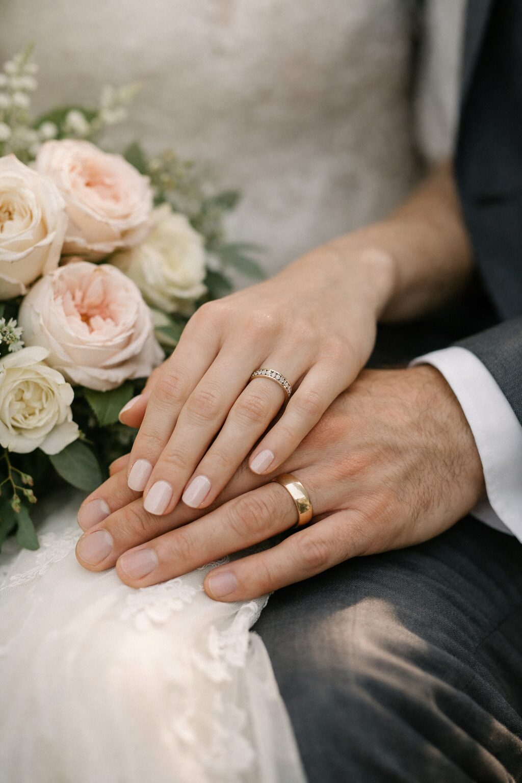 Elegant Wedding Rings and Hands A close-up of a newlywed couple's hands with wedding rings resting on a bouquet of pale pink and white roses. Shot for Lydia Turner.
