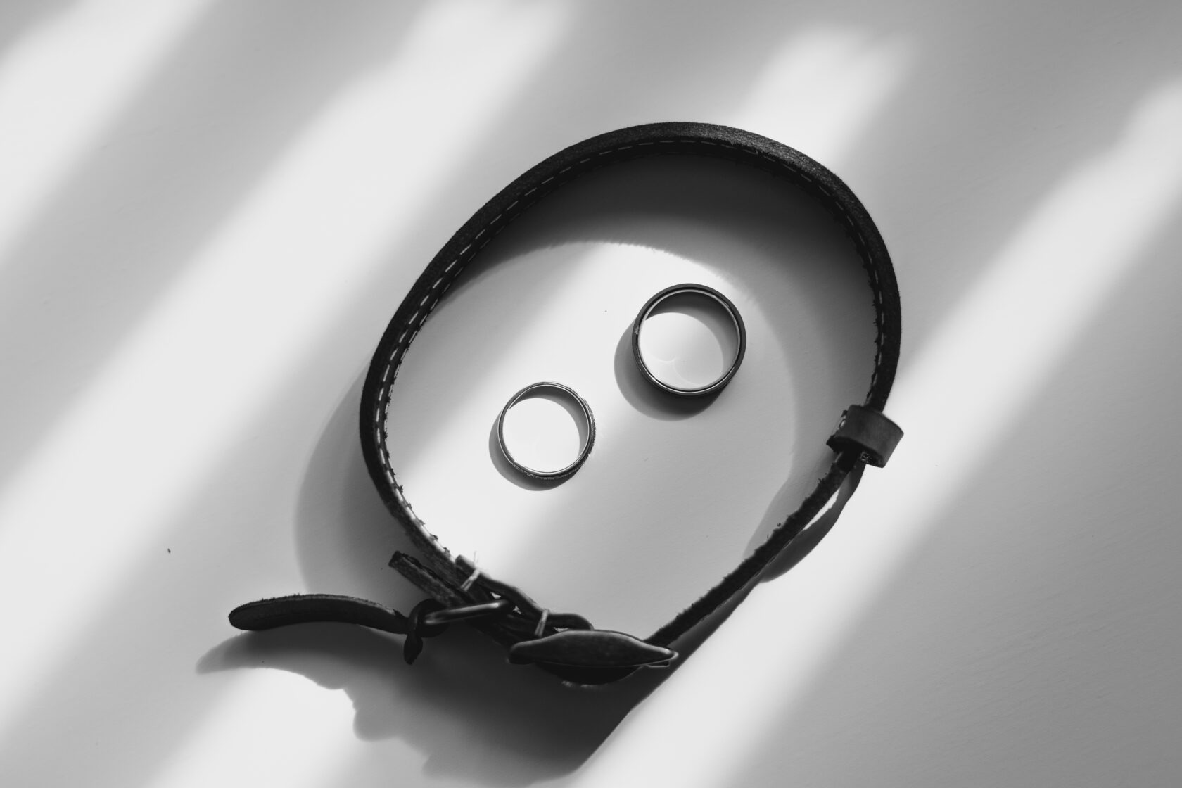 Elegant Rings and Leather Bracelet on Table A close-up view of two metallic rings and a black leather bracelet placed on a light surface, with soft shadows creating a minimalist aesthetic. Shot for Lydia Turner.