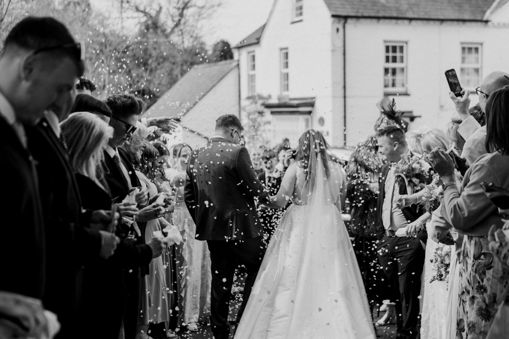 A bride and groom walk through a corridor of guests showering them with confetti, capturing a joyful wedding moment. Shot for Lydia Turner.